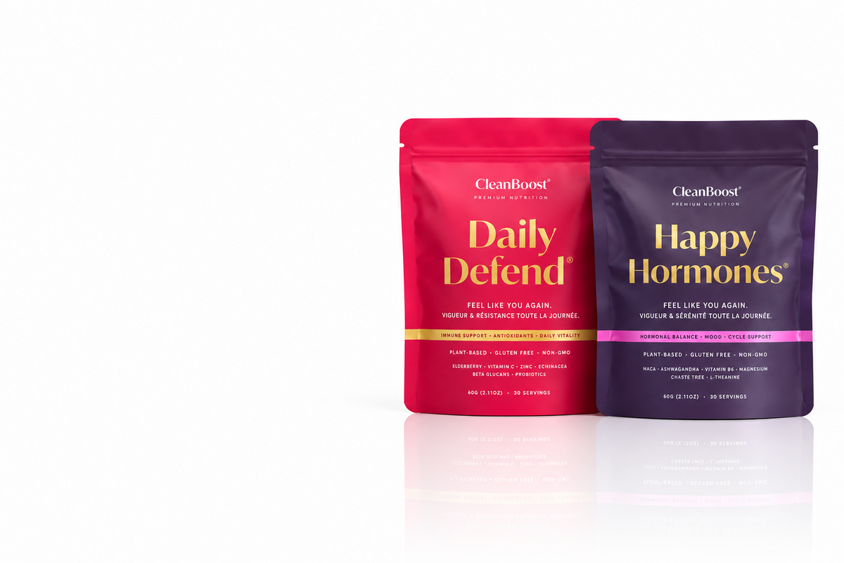 Two stand-up pouches of CleanBoost dietary supplements on a white background: Daily Defend in bright pink with gold lettering, and Happy Hormones in deep purple with gold lettering and a pink band.
